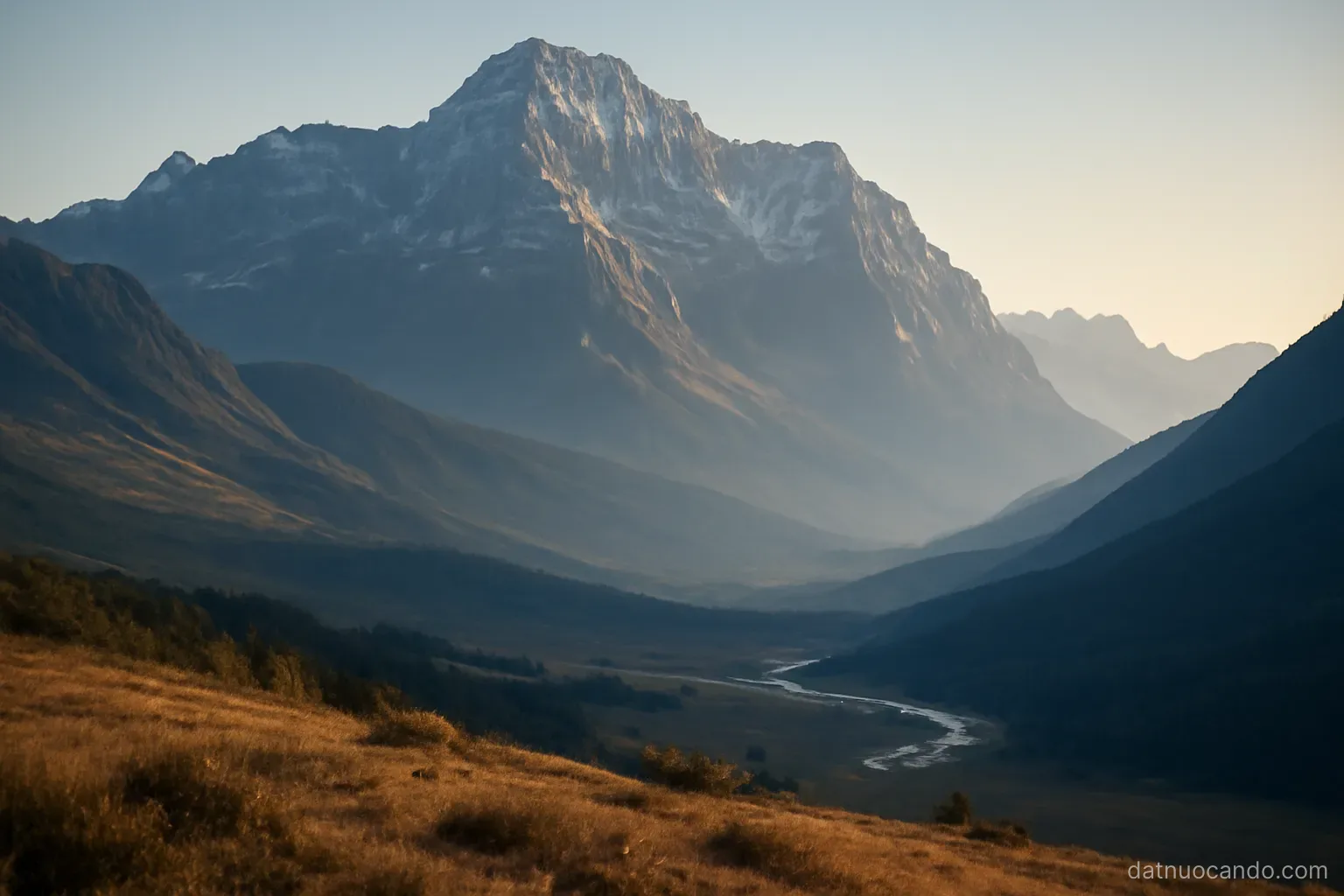 A very high mountain wall seen from a distant foothill, layered ridges receding into haze, a river valley opening below