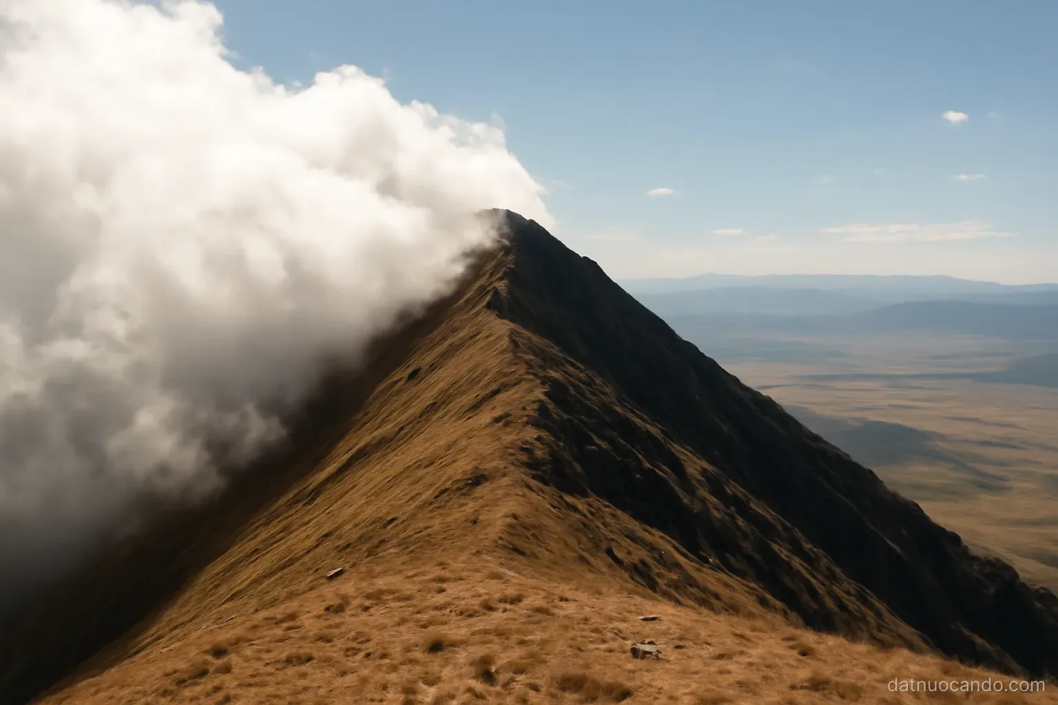 Clouds piling up against one side of a long mountain ridge while the far side stays clear, wide landscape at midday